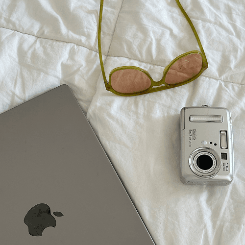 Laptop flatlay on bed with sunglasses and digital camera - Planoly